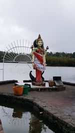 Man standing by statue on lake against sky