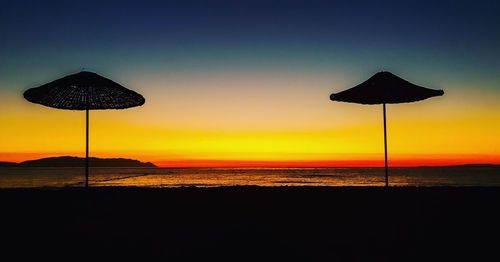 Silhouette parasols on beach against sky during sunset