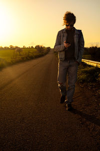 Full length of man standing on road against sunset sky
