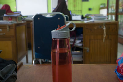 A red water bottle on the desk in the teacher's office