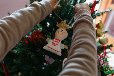 Close up on child hands holding christmas doll decoration putting it on tree