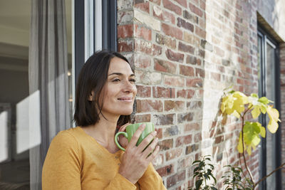 Smiling woman drinking from cup in front of her home