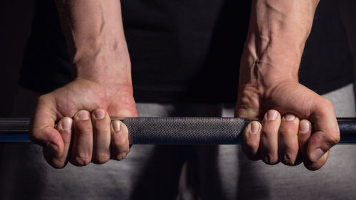 Cropped hands lifting dumbbell in darkroom