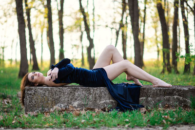 Woman lying down on land against trees in forest