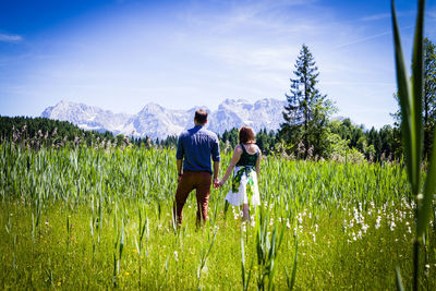 Rear view of couple standing on grassy land against sky