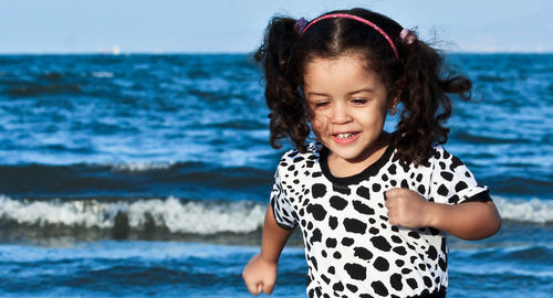 Smiling cute girl running against sea at beach