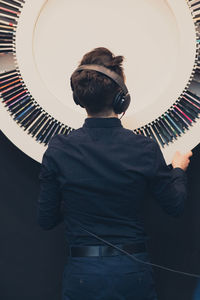 Rear view of teenage boy listening music while standing against decoration