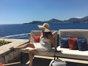 Woman sitting on chair by sea against sky