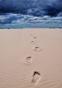 Footprints at beach against cloudy sky