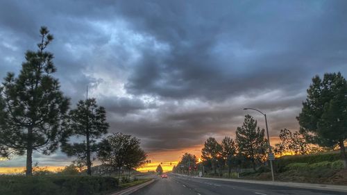 Road by trees against dramatic sky