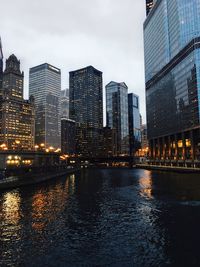 Illuminated buildings by river against sky in city