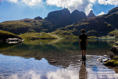 Rear view of man standing by lake against mountains