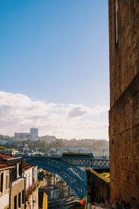 Bridge amidst buildings against cloudy sky in city during sunset