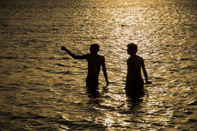 Silhouette people standing in sea against sky during sunset