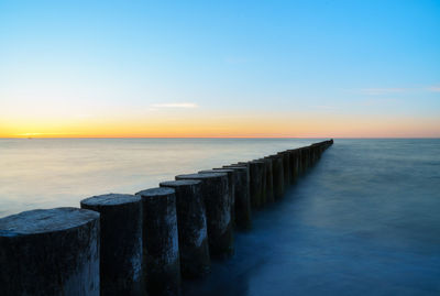 Wooden posts in sea against sky during sunset