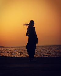 Woman standing by sea at sunset