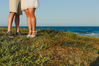 Low section of couple standing on field against sea