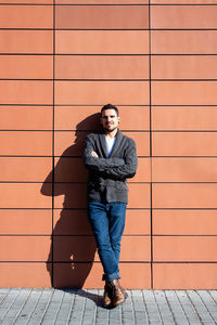 Front view of a fashionable young man standing against orange wall