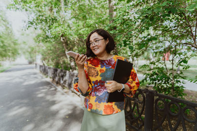 Joyful woman with smart watch and laptop talking on the phone on day in the park