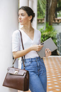 Smiling woman holding book looking away standing outdoors