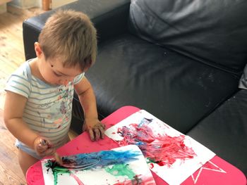 High angle view of baby boy painting on paper at home