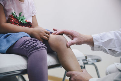 Cropped hands of mature male doctor examining girl's knee at hospital
