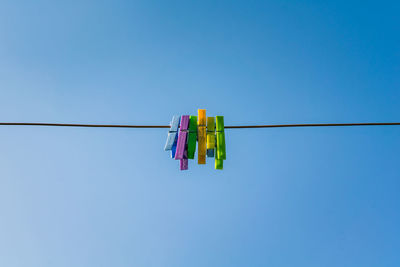 Low angle view of clothespins hanging on clothesline against blue sky