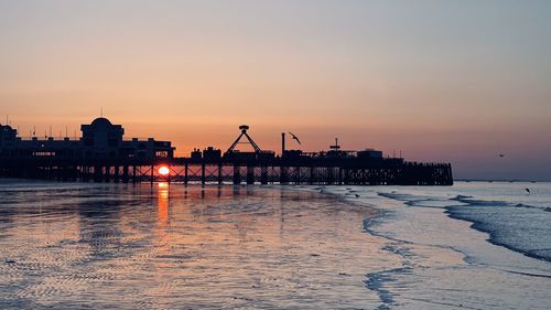 Silhouette cranes by sea against sky at sunset
