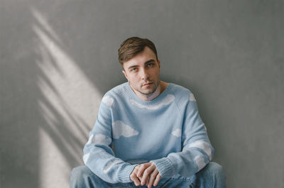 Portrait of young man sitting against wall