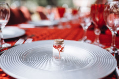 A small red flower in small jar stands on a silver plate against the background of a red tablecloth