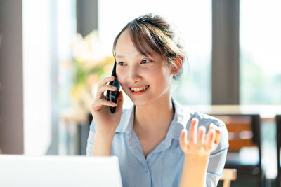 Young woman using mobile phone while sitting on table