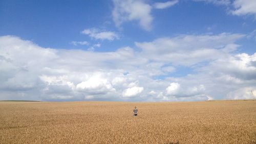 Mid distance of man standing on wheat field against cloudy sky
