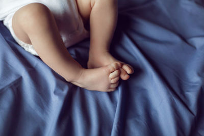 Close up leg baby boy blonde in white bodysuit lying on the bed