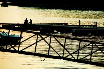 Silhouette people standing at riverbank against sky during sunset