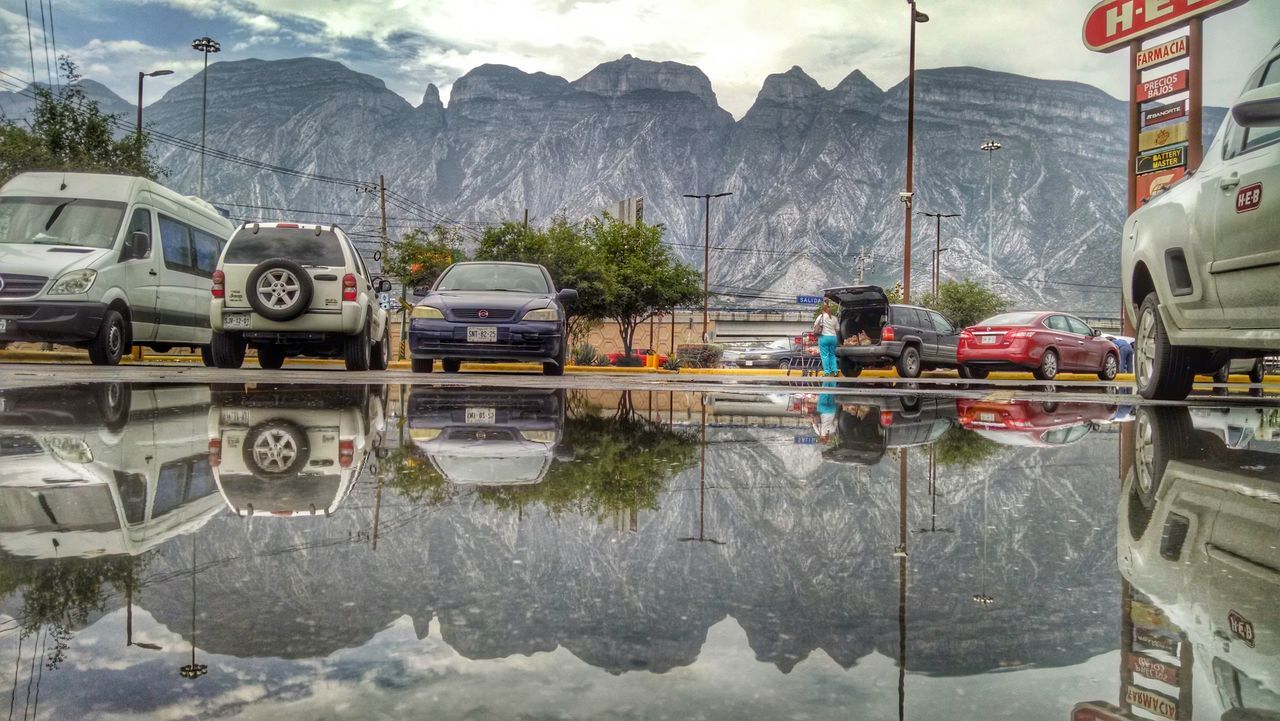 transportation, mode of transport, mountain, sky, nautical vessel, cloud - sky, moored, text, day, car, building exterior, travel, outdoors, incidental people, boat, water, harbor, built structure, land vehicle, western script