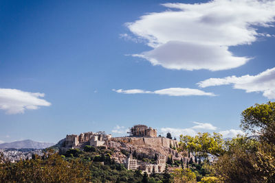 Built structures on landscape against blue sky and clouds