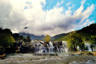 Scenic view of waterfall against cloudy sky