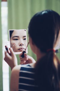 Reflection of woman applying make-up in mirror at home
