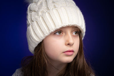 Smiling girl wearing knit hat looking away against purple background