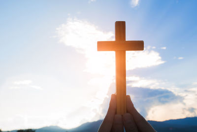 Hand of cross against sky during sunset