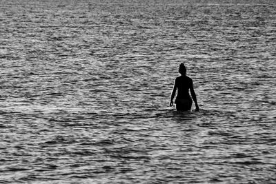 Silhouette of a woman from behind walking in the shallow water at the beach