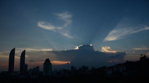 Silhouette of city against cloudy sky during sunset