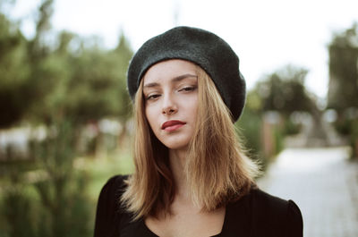 Close-up portrait of young woman wearing hat standing against sky at park