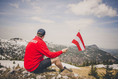 Rear view of woman sitting on mountain against sky