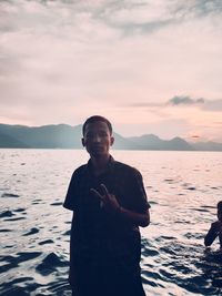 Young man standing at beach against sky during sunset