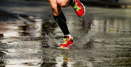 Low section of man splashing water while running on puddle