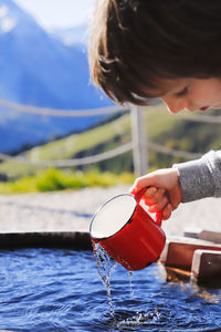 Boy filing mug with water outdoors