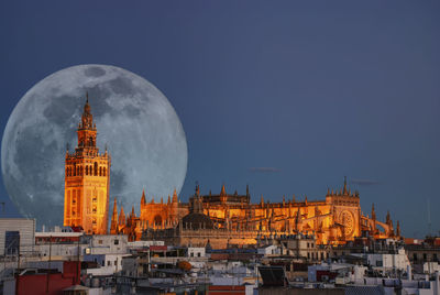 A full moon behind the illuminated cathedral in seville, spain