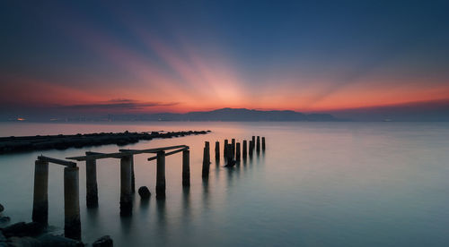 Wooden posts in sea against sky during sunset