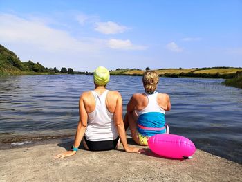 Rear view of friends sitting on shore against sky